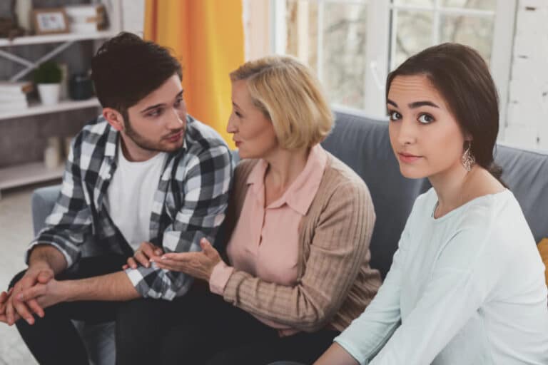 Young woman sitting quietly at the family table while her mother serves her adult brother